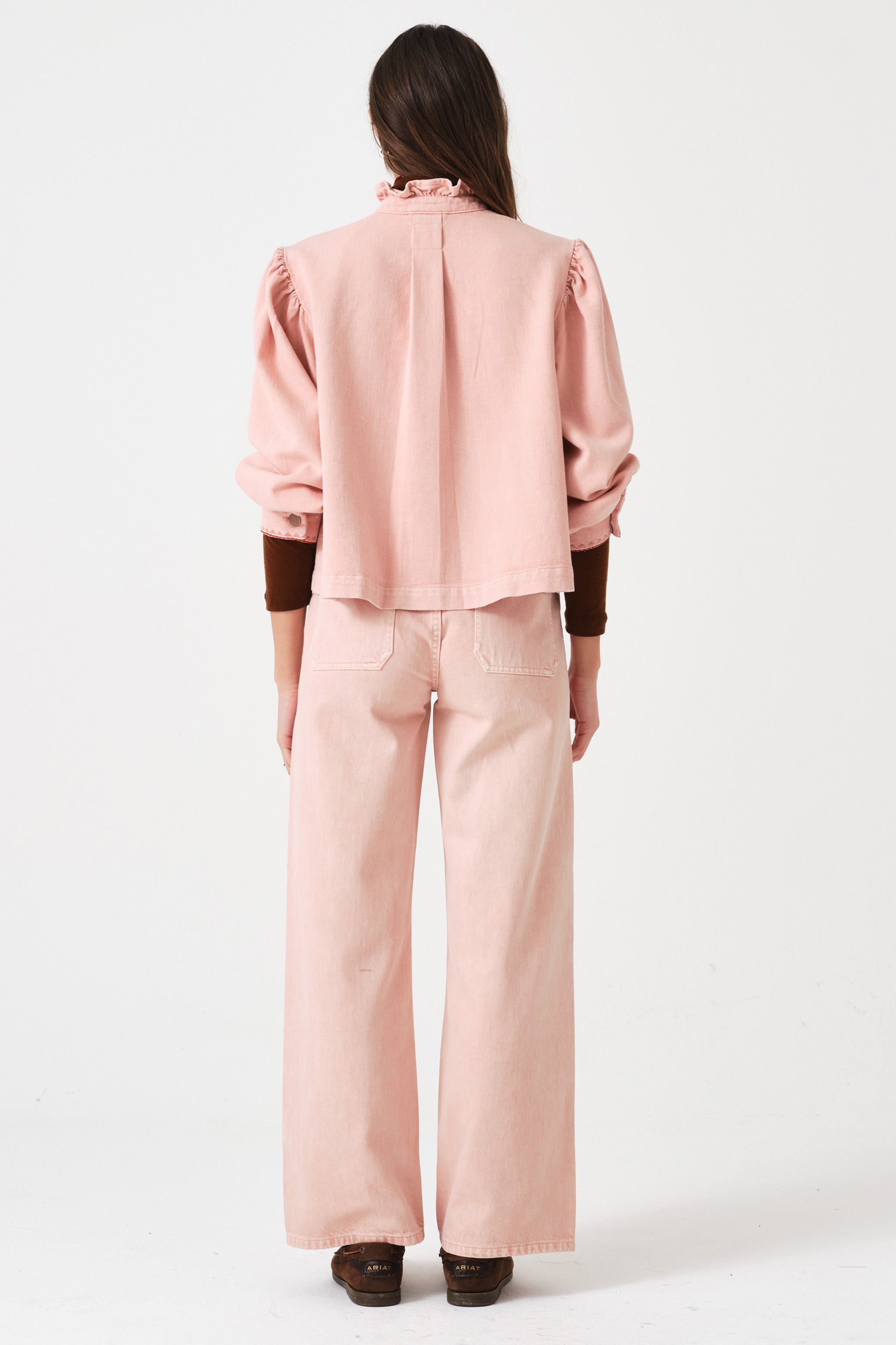 woman wearing light pink high waisted, wide, cropped jeans with big pockets, a pink shirt, and brown shoes on a white background
