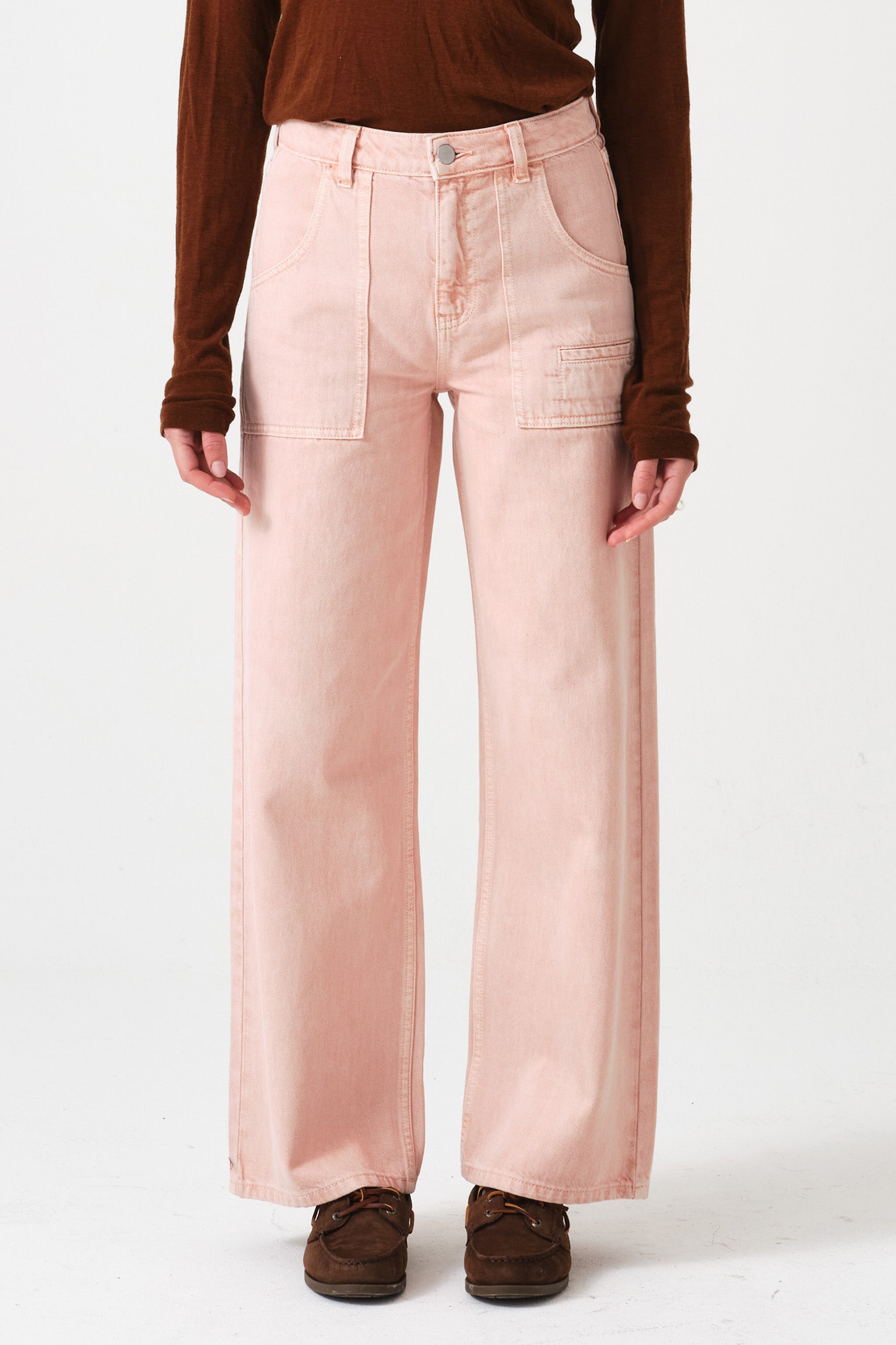 woman wearing light pink high waisted, wide, cropped jeans with big pockets and brown shoes on a white background
