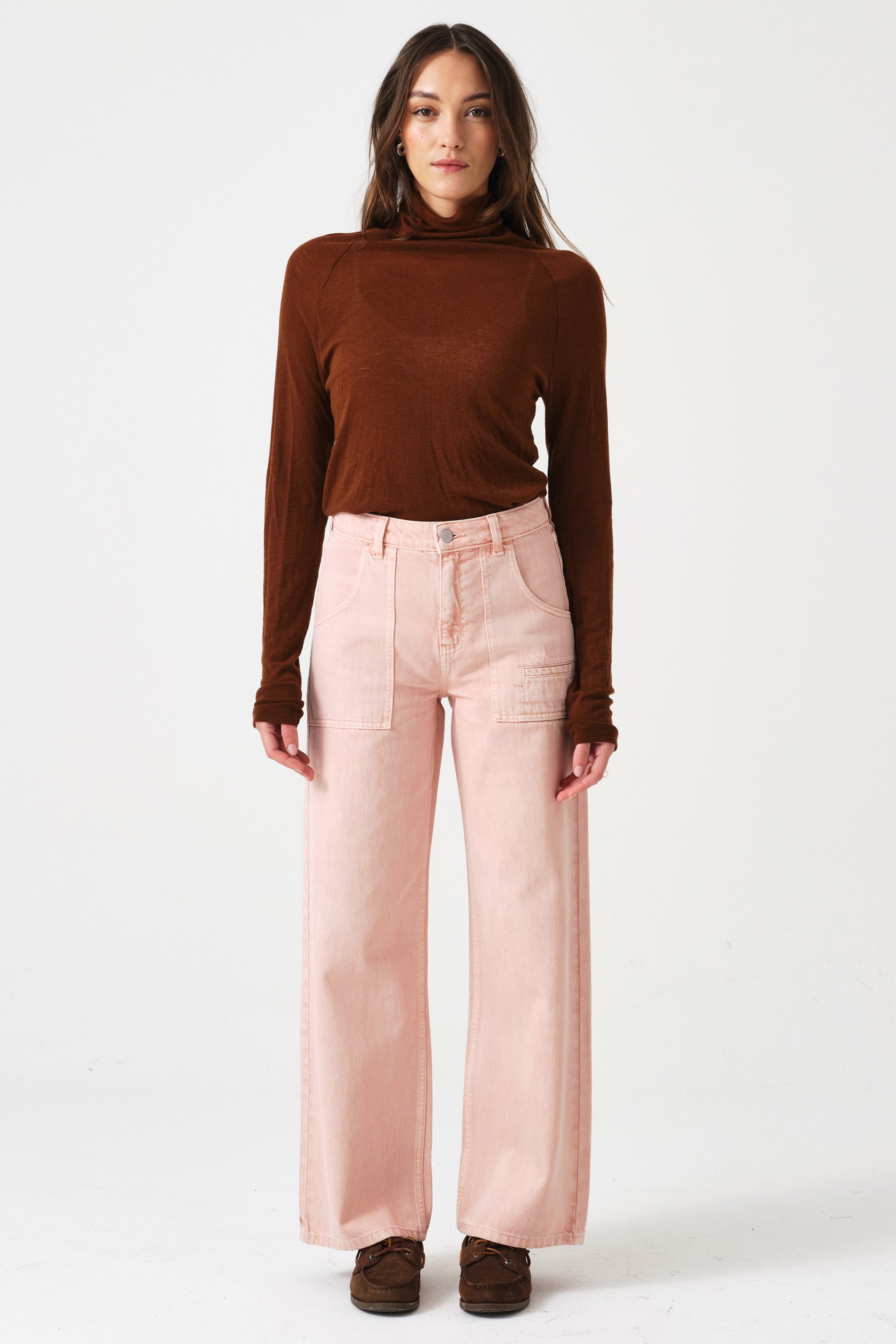 woman wearing light pink high waisted, wide, cropped jeans with big pockets, a brown shirt, and brown shoes on a white background