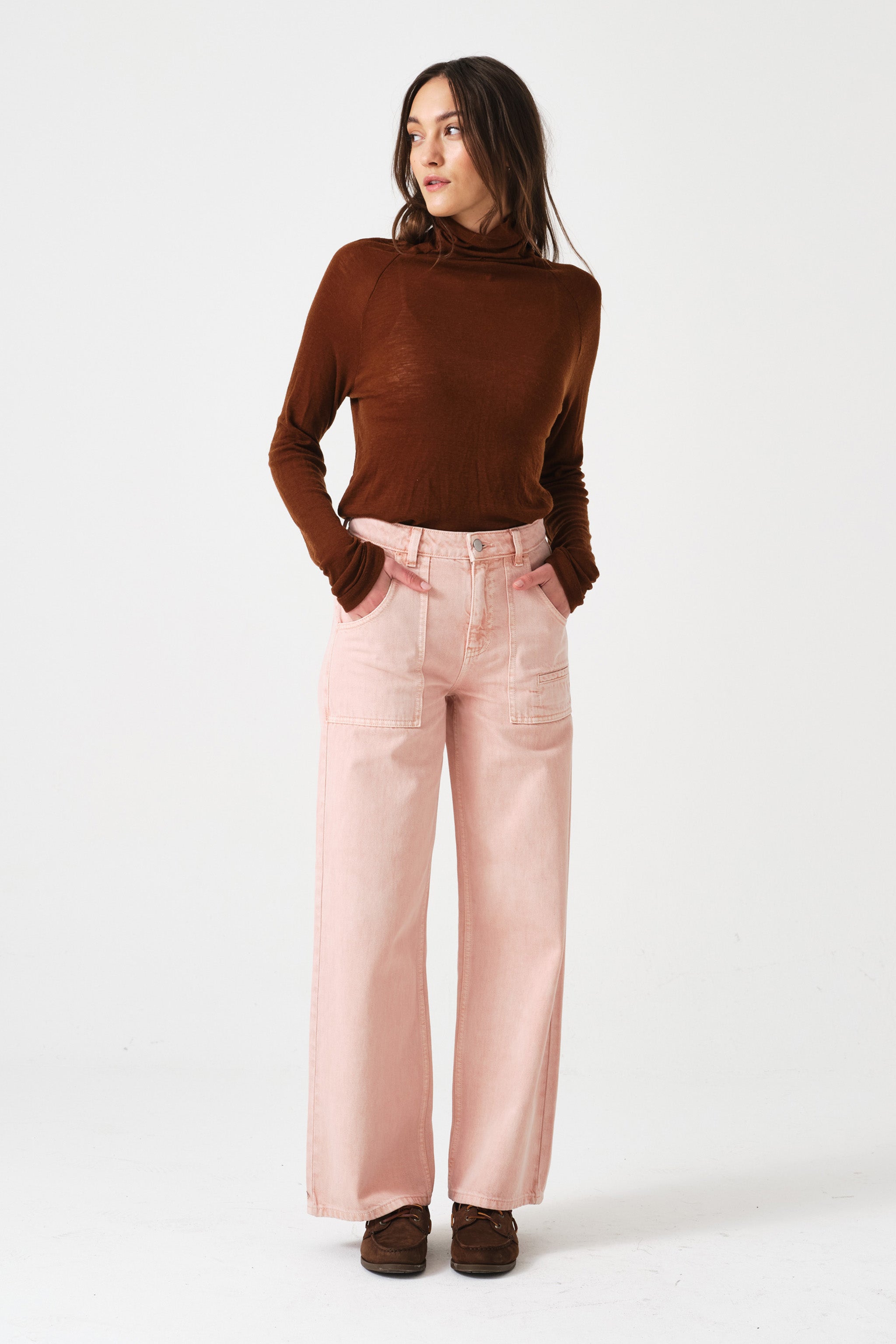woman wearing light pink high waisted, wide, cropped jeans with big pockets, a brown shirt, and brown shoes on a white background