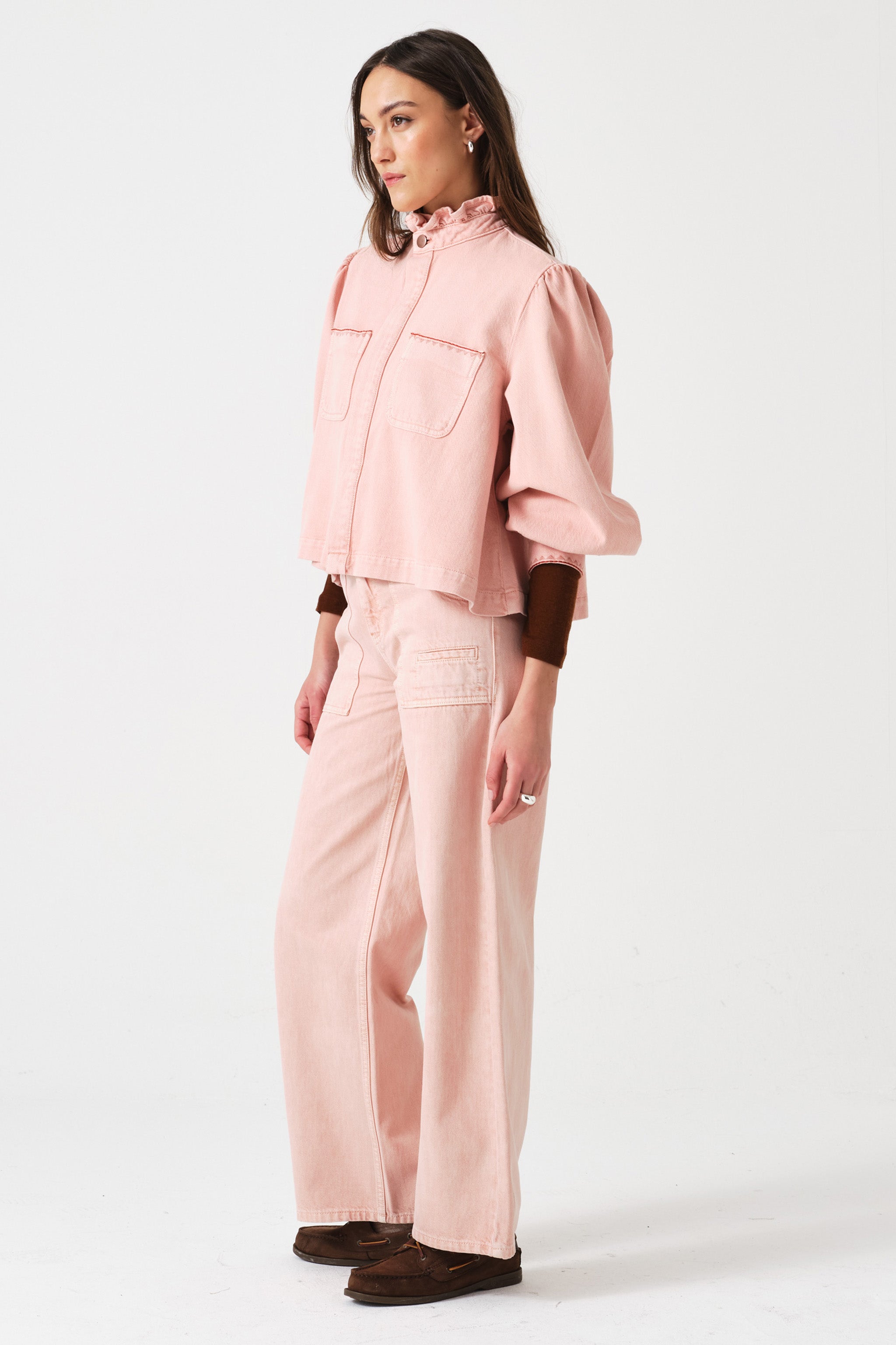 woman wearing light pink high waisted, wide, cropped jeans with big pockets, a pink shirt, and brown shoes on a white background