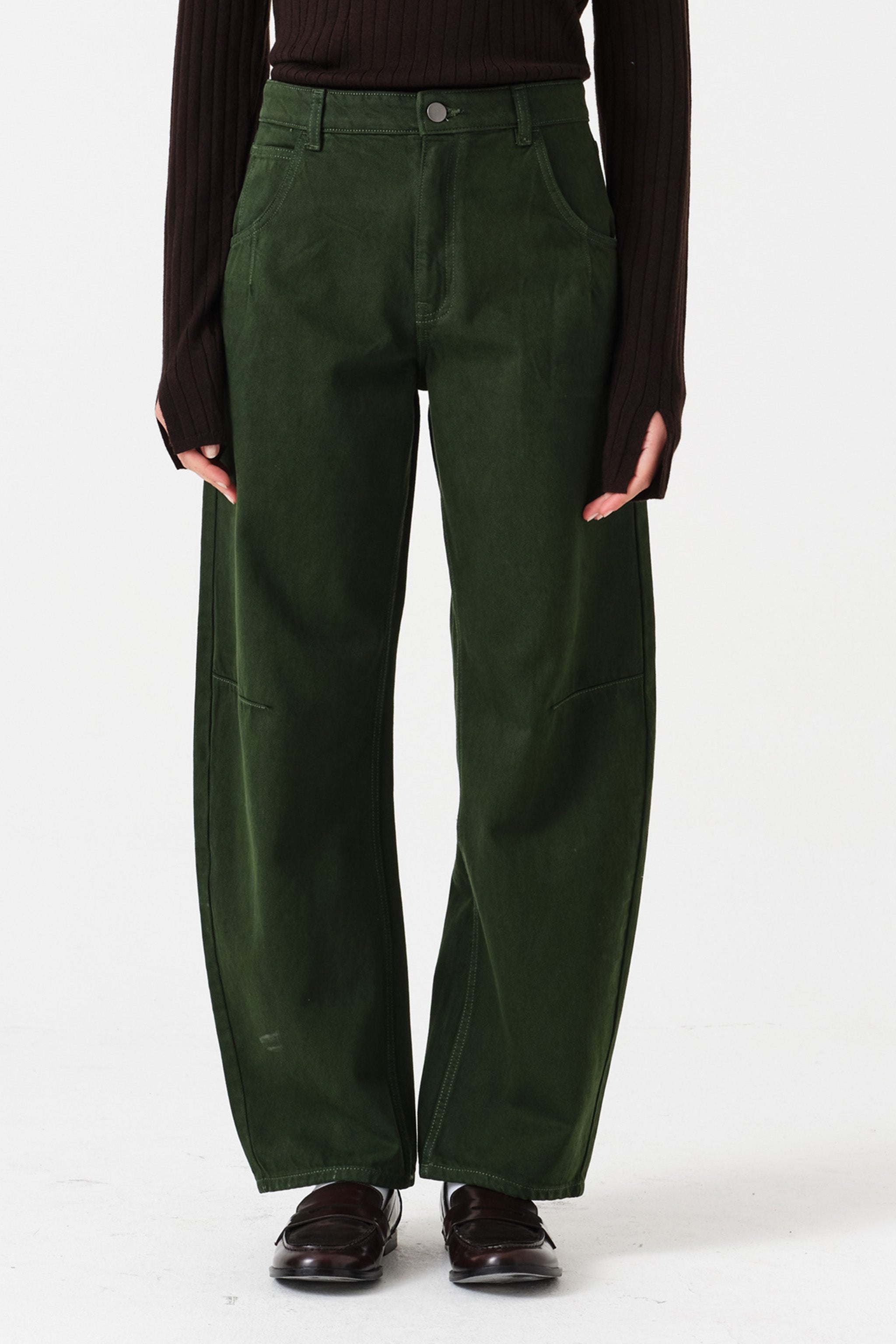 Woman wearing dark green barrel leg jeans and a brown shirt on a white background