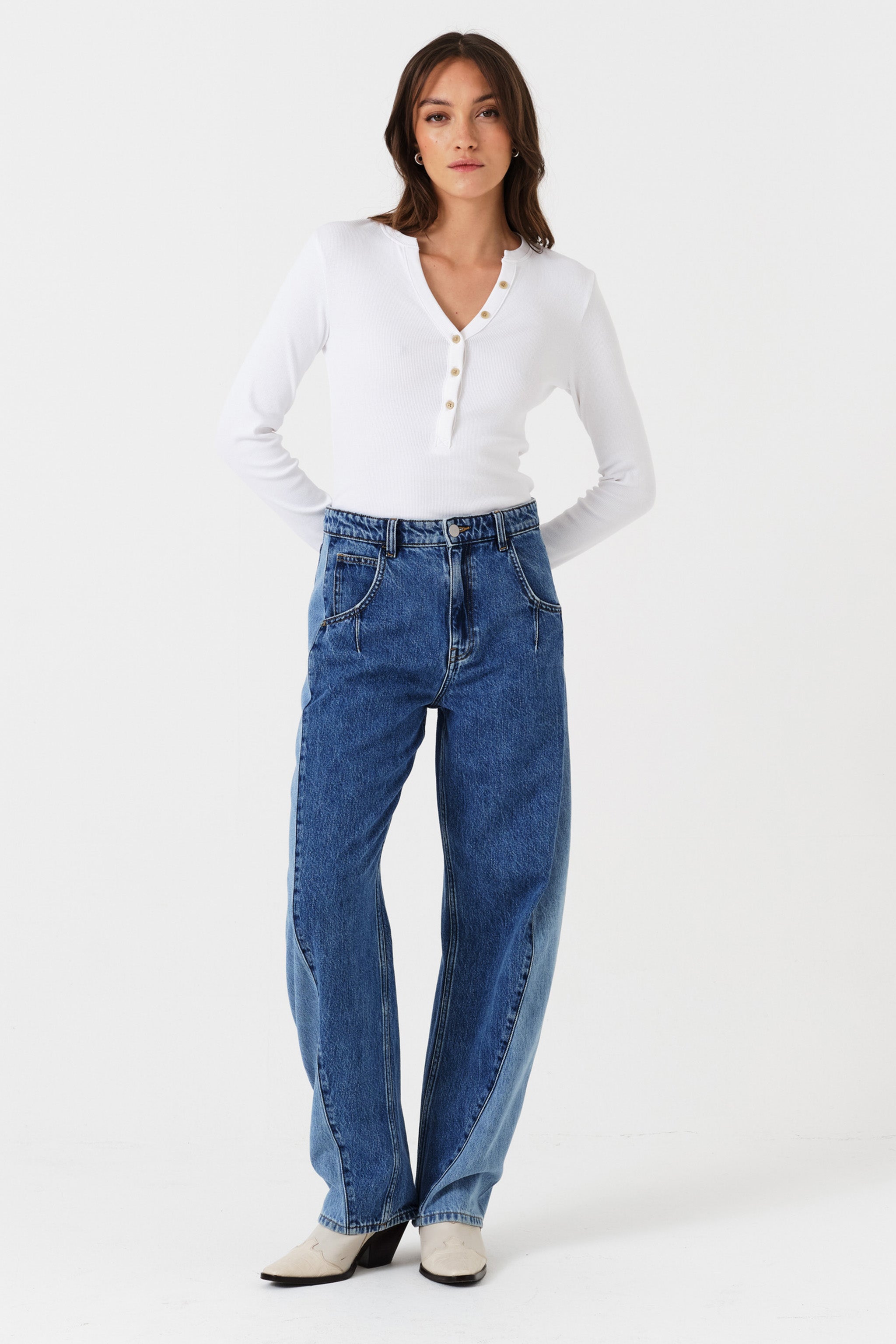 Woman wearing two toned blue barrel leg jeans and a white shirt on a white background front view